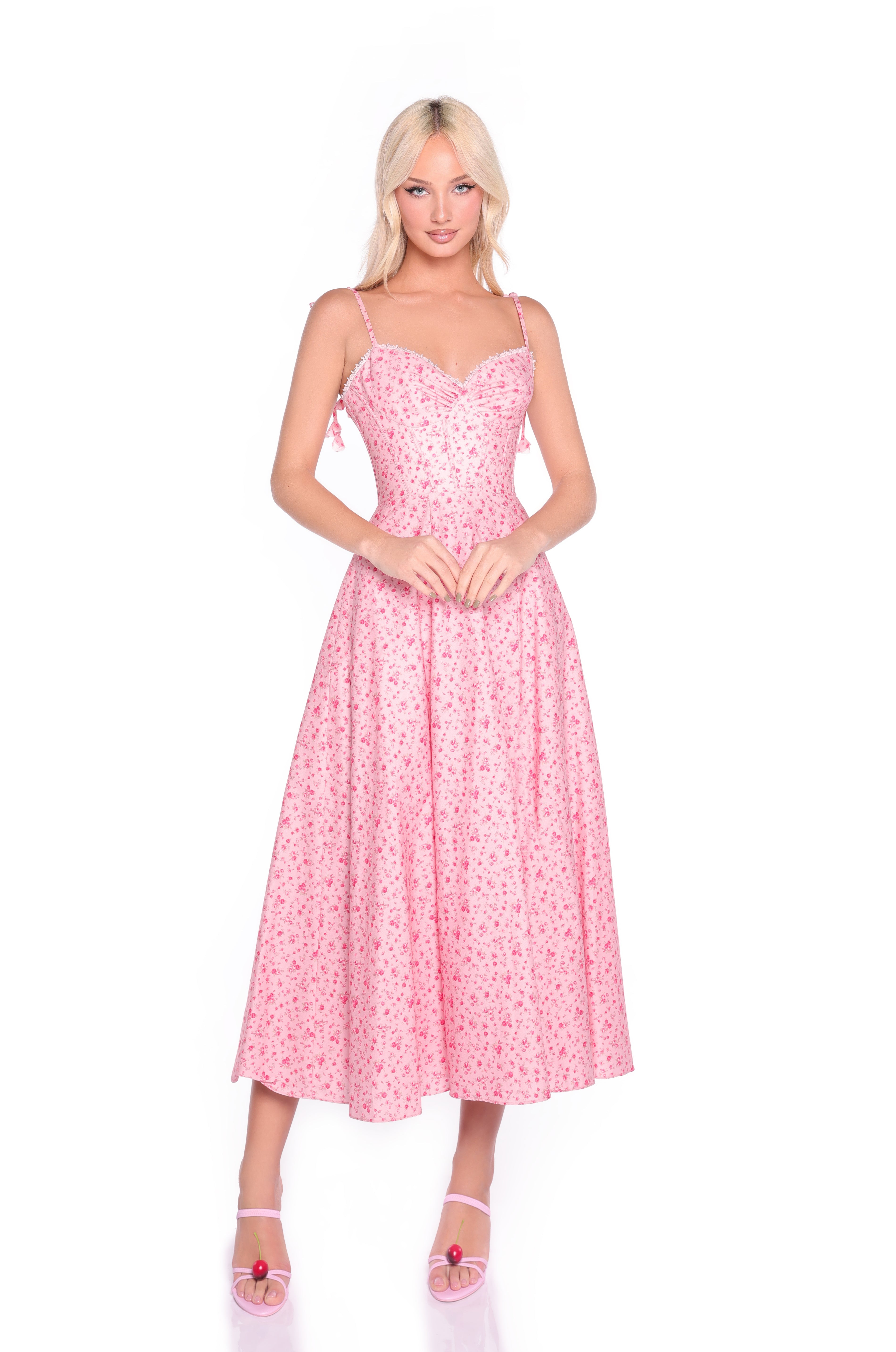 Woman in the Aria Casual Midi Pink Floral Dress with a corset bodice and spaghetti straps, paired with pink heeled sandals, stands against a white background—ideal for casual dress occasions.